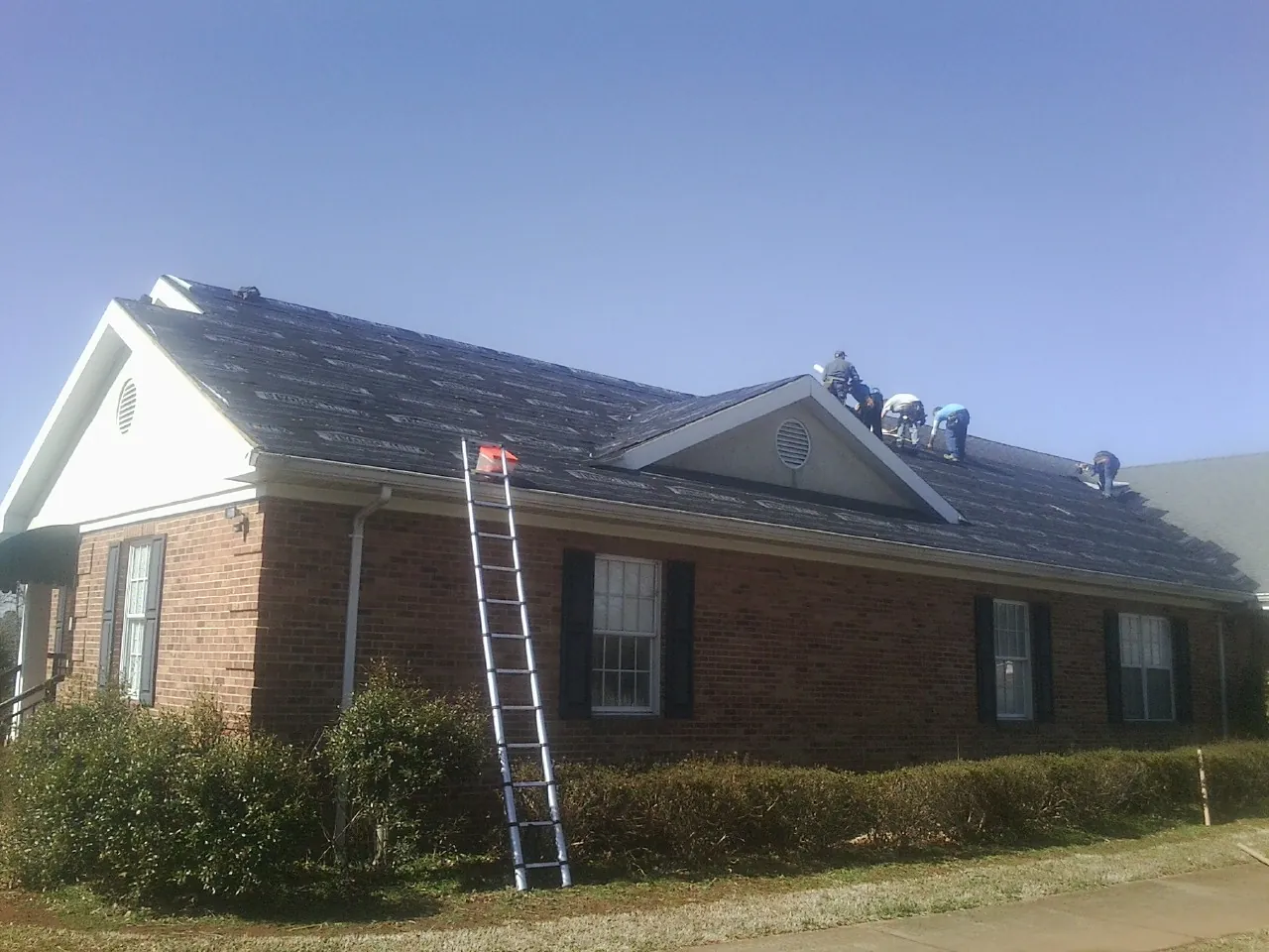 Crew tearing shingles off a brick ranch roof with a ladder set — Emergency Roof Repair work by our crew in Penn Laird