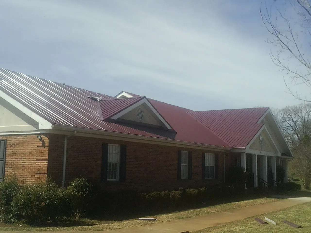 Red metal roof with gabled entries on a long brick building, from a Hail Damage Roof Repair job in Penn Laird