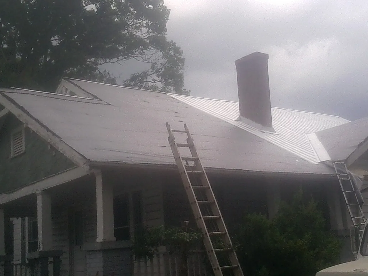 Ladders against a metal roof on an older home with a brick chimney in Penn Laird