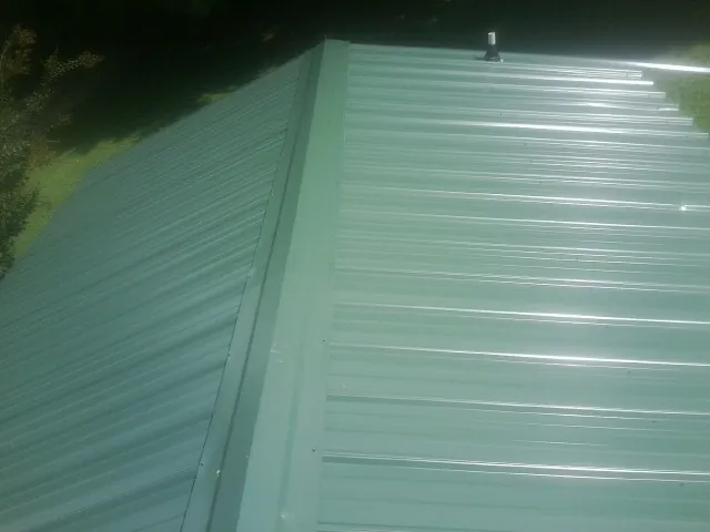 New green metal panels meeting at the ridge of a roof — Flat Roof Repair work by our crew in Penn Laird