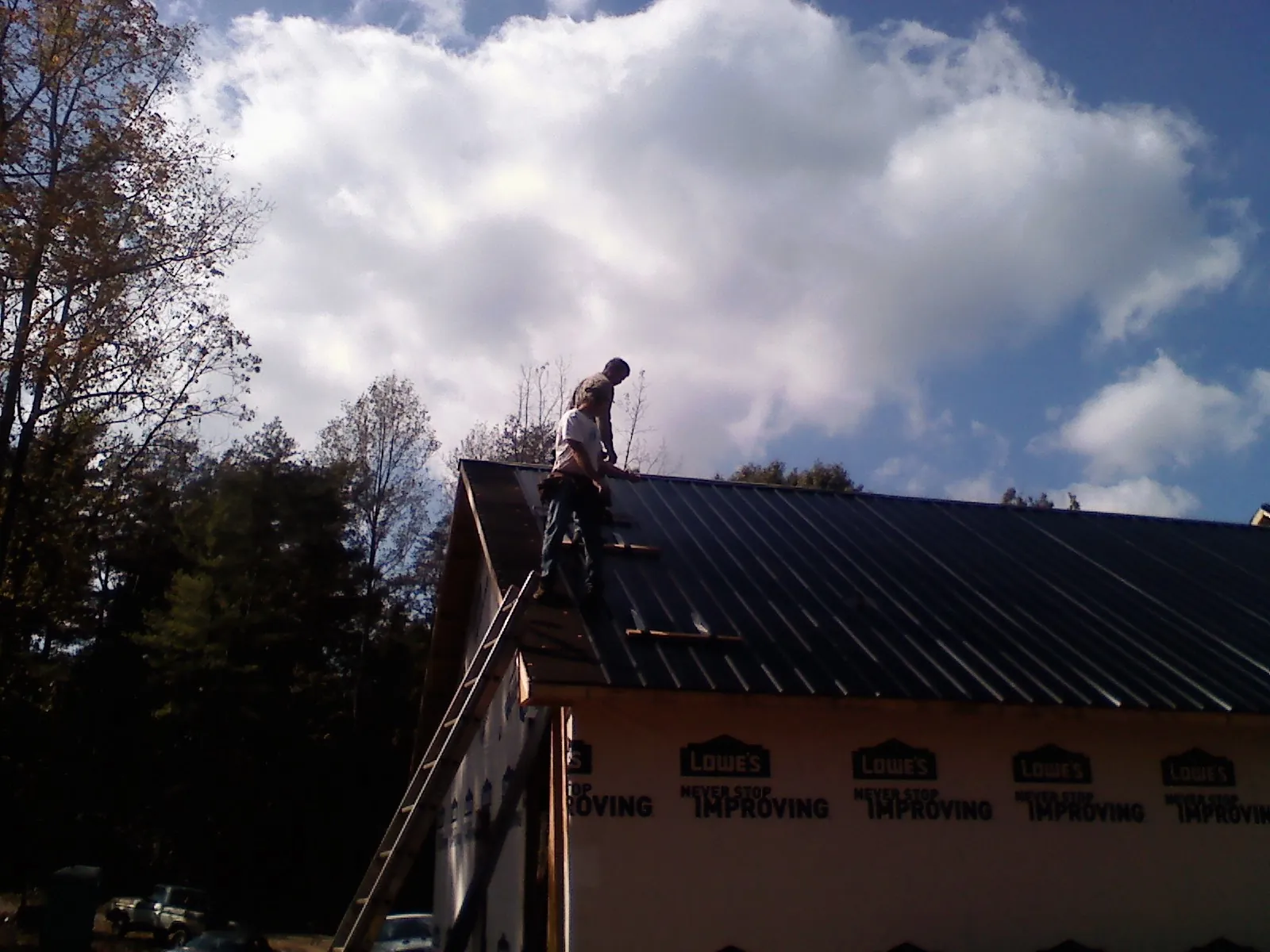Roofer fastening dark metal panels high against a cloudy sky, from a Roof Inspection job in Penn Laird