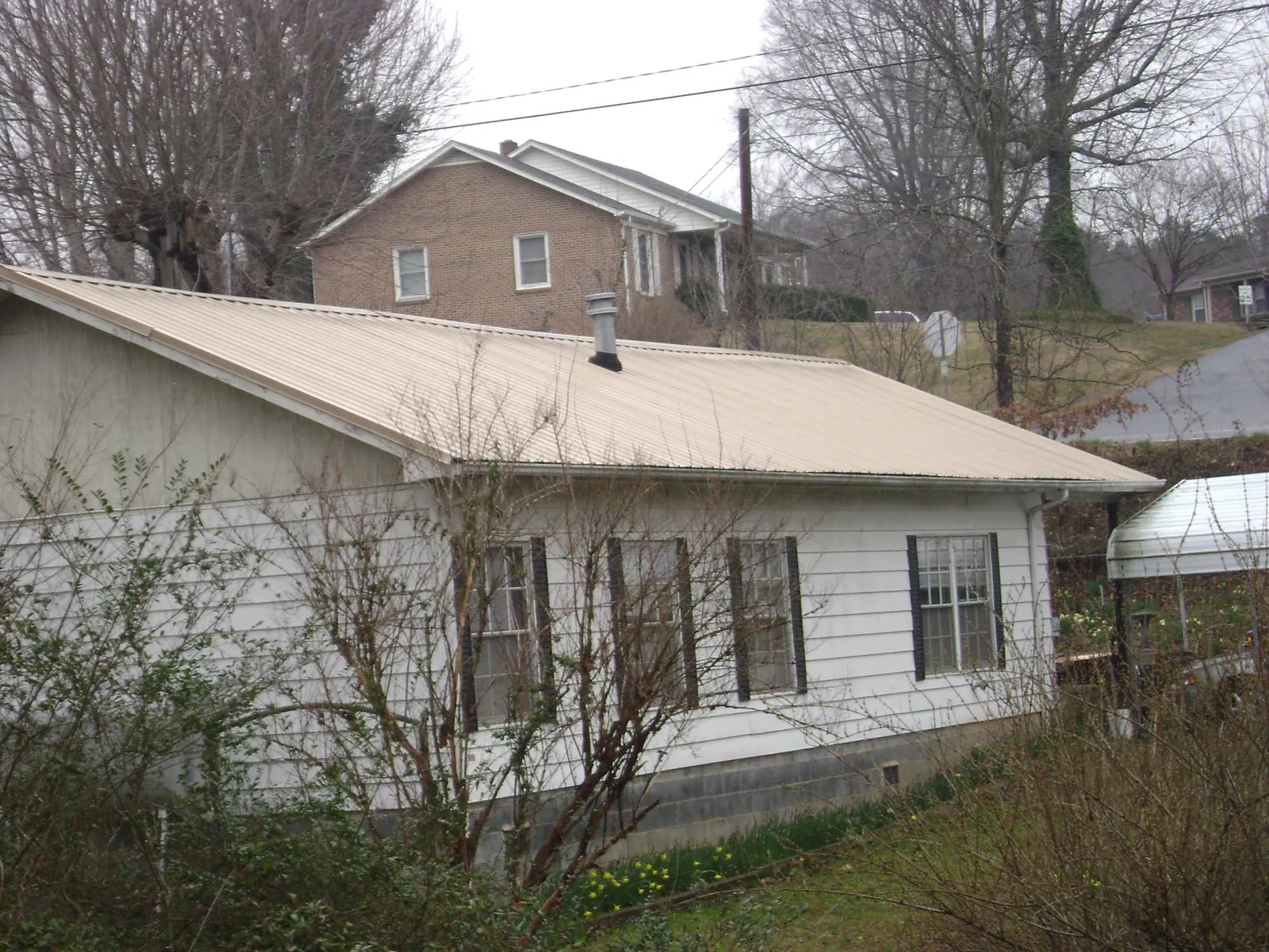 Tan metal roof on a white sided house set into a hillside — Commercial Roofing by Roofing Brothers in Penn Laird