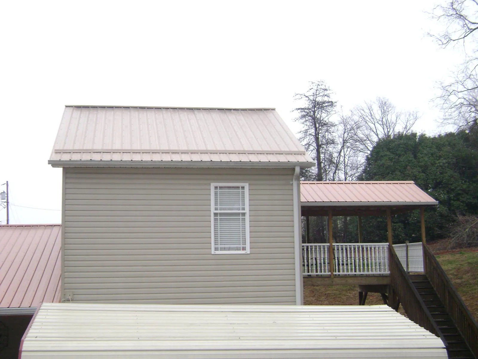 Tan metal roofs on a two story addition and attached porch, from a Roof Replacement job in Penn Laird